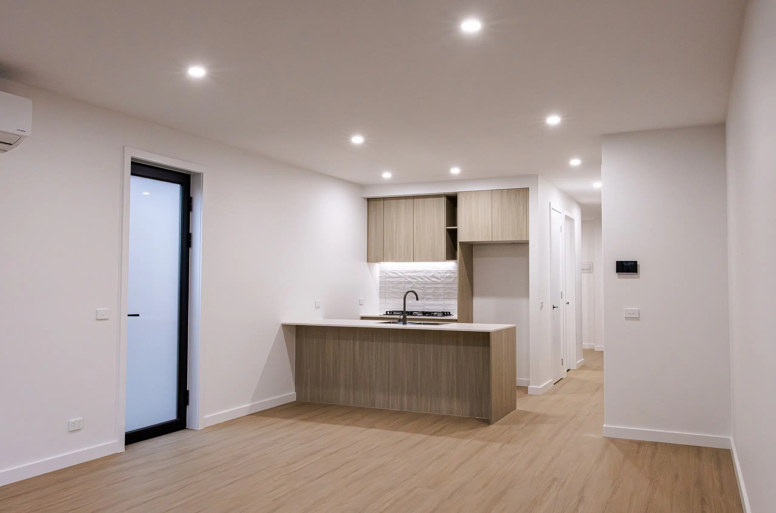 Empty room with a timber floor, white walls and a compact kitchen, shot for a real estate listing