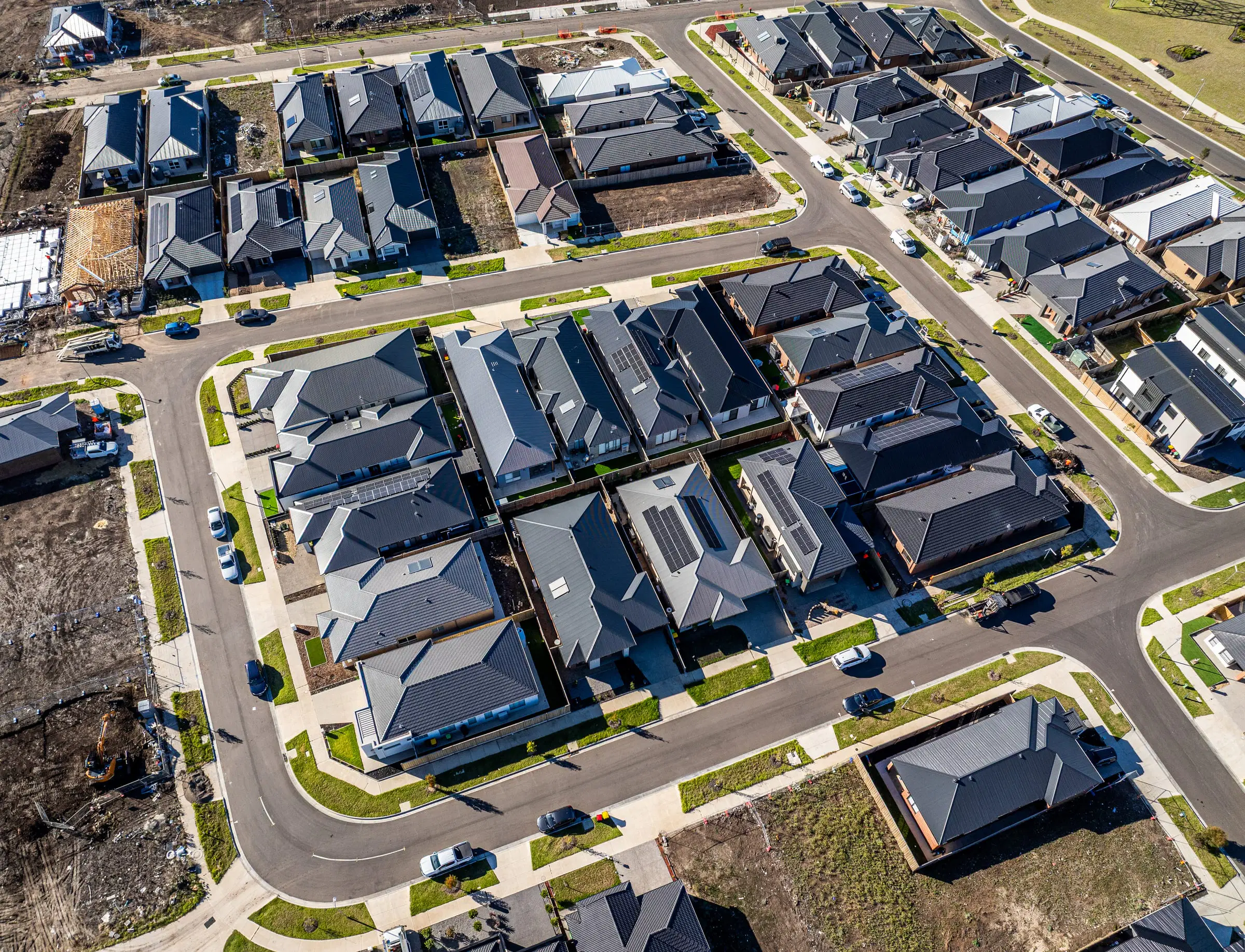 Drone view over a new housing estate, rows of dark roofs along curving streets