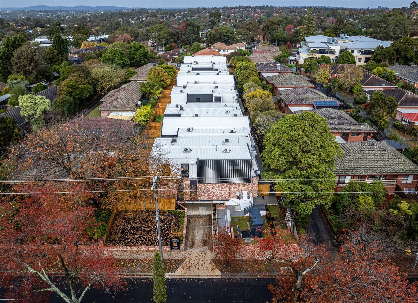 Drone view of a townhouse development among trees and neighbouring homes